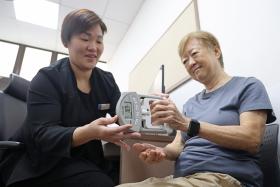 Retired secretary Doris Yam doing a hand grip test under the supervision of Ms Doreen Chan, a senior care coordinator at NHG polyclinics.