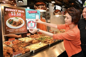 Senior Minister of State for Trade and Industry Low Yen Ling pasting decals on a stall at a coffee shop run by private chain operator Chang Cheng. 