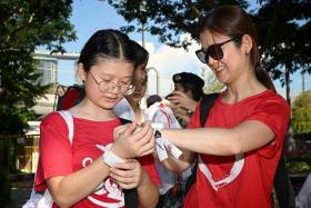 Kiara Phang, 12, putting on an NDP wristband with the help of her mother, Ms Celine Hsieh, 40, at the Padang on Aug 3.