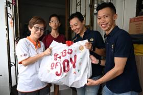 (From left) Beneficiaries Jane Lim and her son Yew Zhe Hao receiving a &quot;bags of joy” goodie bag from financial advisers Chew Shu Xiang and Samuel Koh.